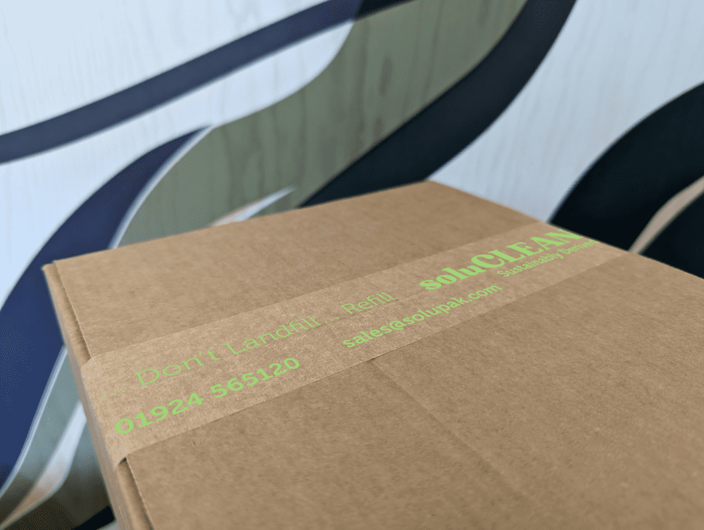 Closed corrugated cardboard box with branded kraft paper tap stating 'soluCLEAN' in green text sealing two flaps