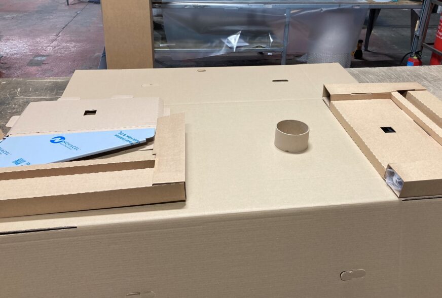 A bespoke packaging solution for a Pland Stainless sluice sink. The wrap is opened, with end caps and cardboard core in position on the central panel ready to assemble.