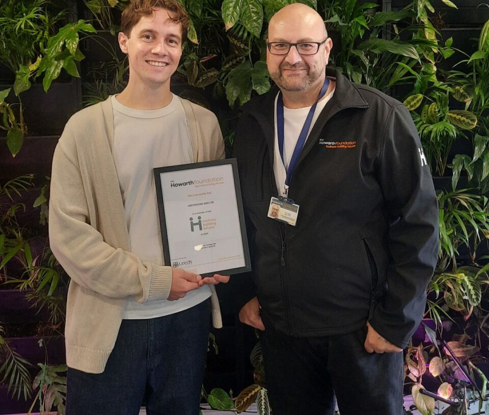 A member of the Greyhound Box team holding a certificate next to a member of The Howarth Foundation team