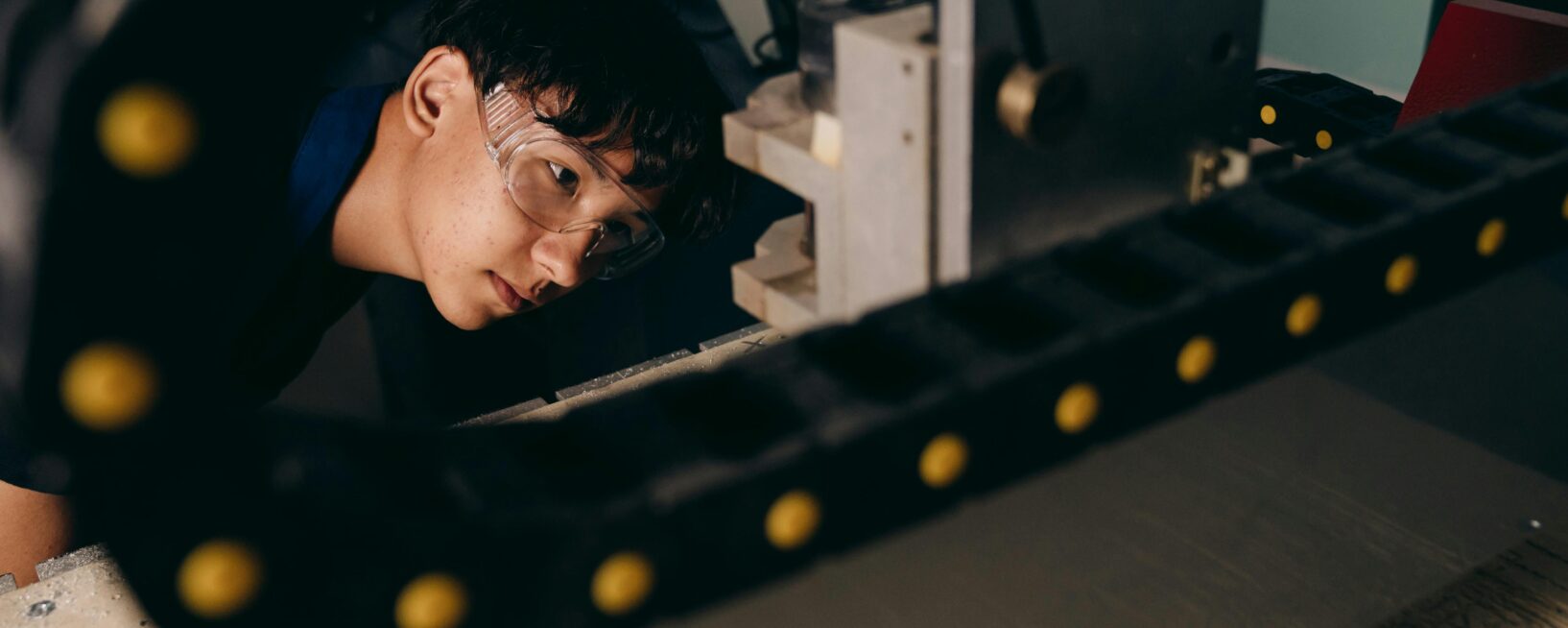 Student manufacturer wearing goggles looking at a chain on a machine