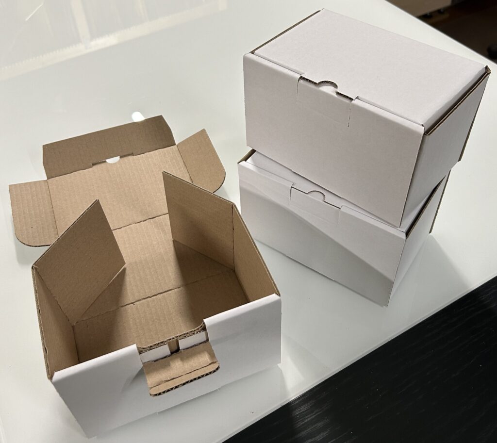 3 white corrugated cardboard boxes. 2 are closed and stacked on top of each other and one is open.